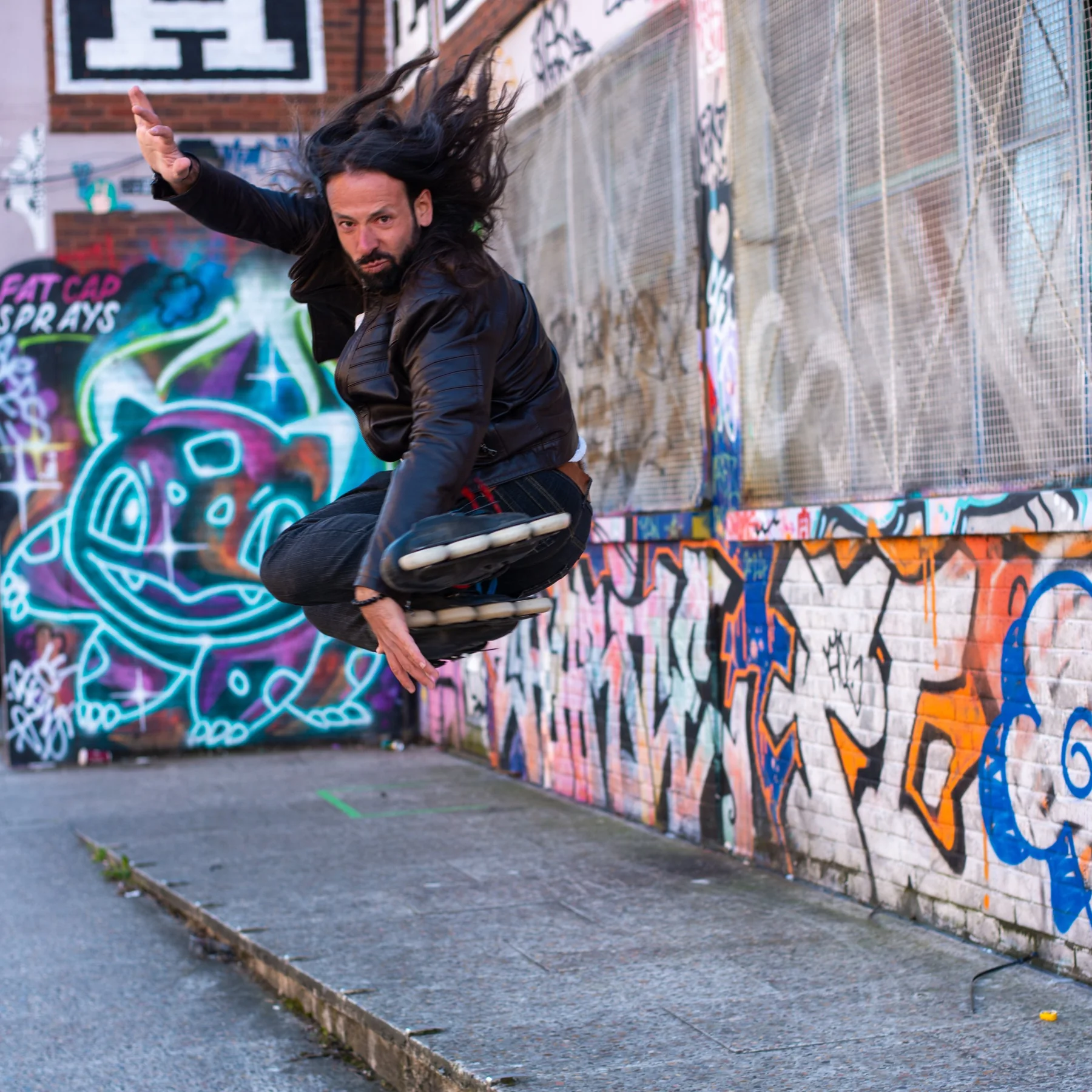 Adrian jumping on inline skates beside a graffiti-covered wall